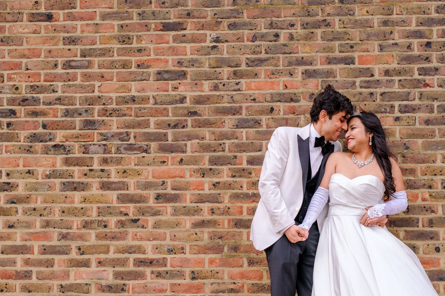 Wedding couple embracing against rustic brick wall background.