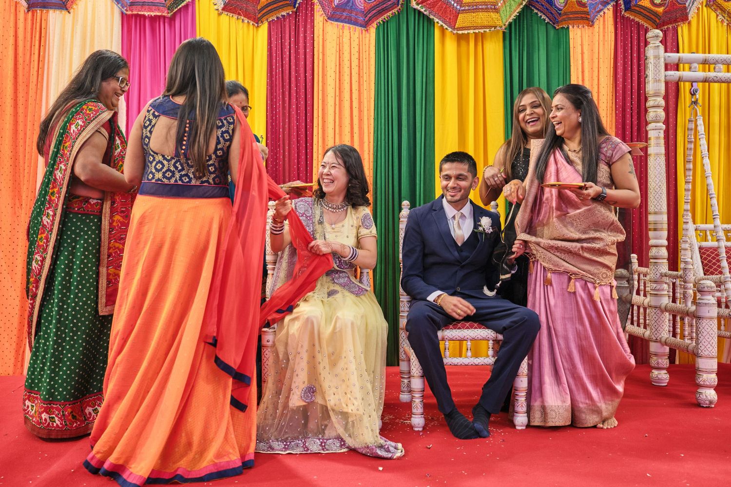 Colorful Indian wedding ceremony backdrop with orange, pink, and green draped fabric panels and decorative elements.