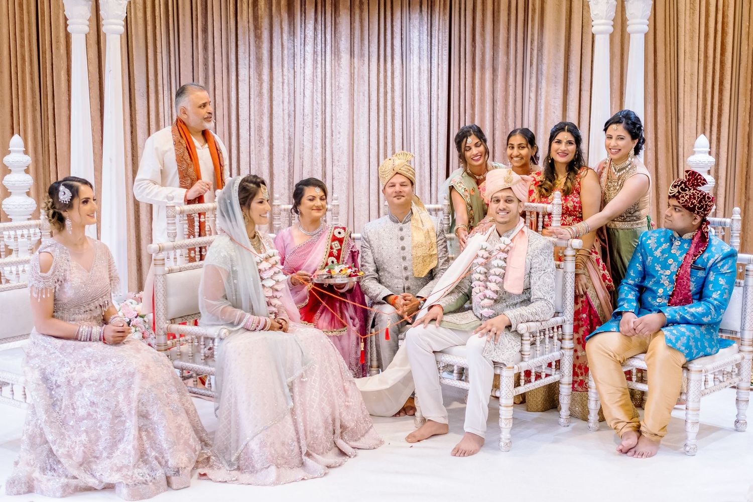 Wedding guests seated in white chairs at an elegant indoor venue with pillared decor.