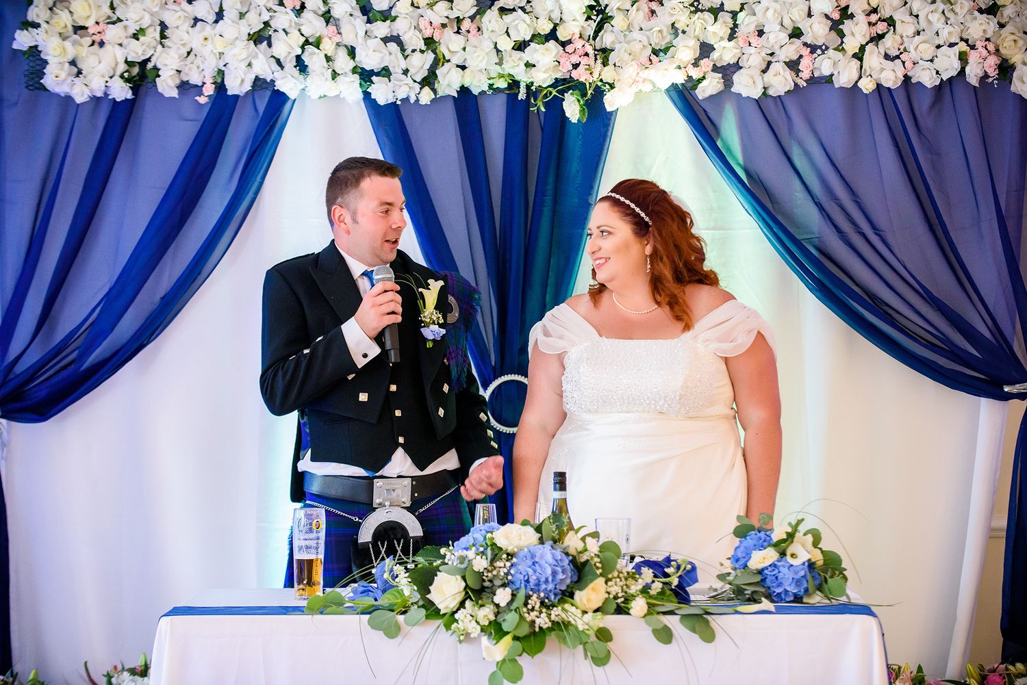 Wedding reception venue decorated with blue drapes and white floral arrangements.