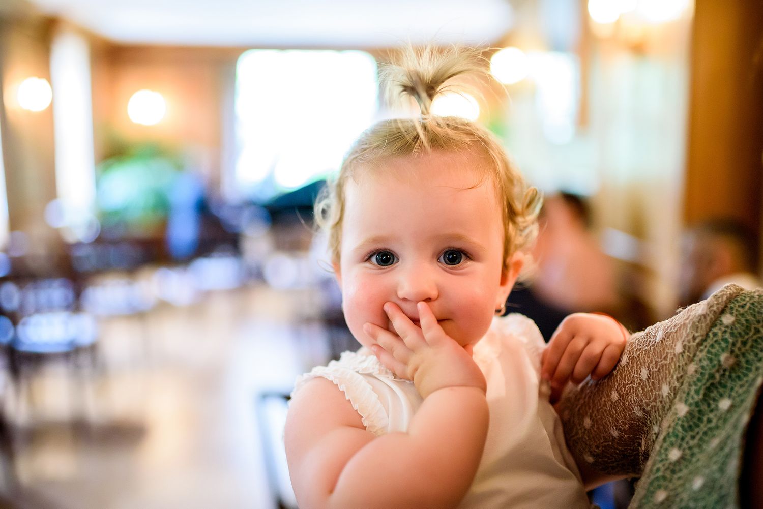 Baby reaches out while being held during indoor celebration.