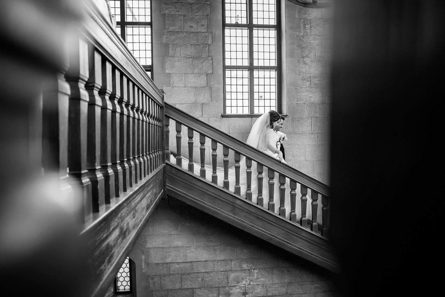 Black and white photo of figure ascending grand staircase with dramatic window lighting.