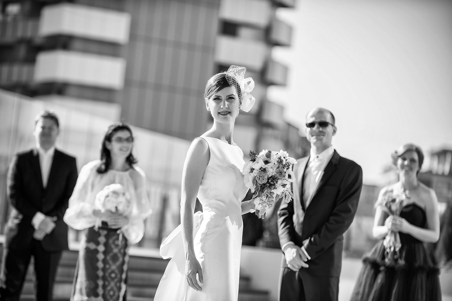 Wedding ceremony guests gathered on a modern rooftop venue against a bright sky.