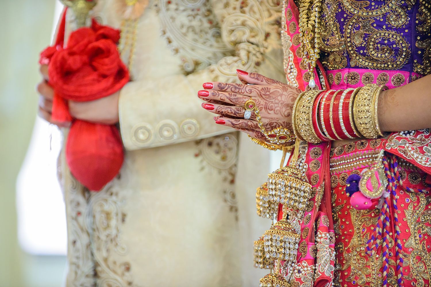 Close-up of ornate bridal jewelry and henna-adorned hands with traditional red and gold wedding attire.