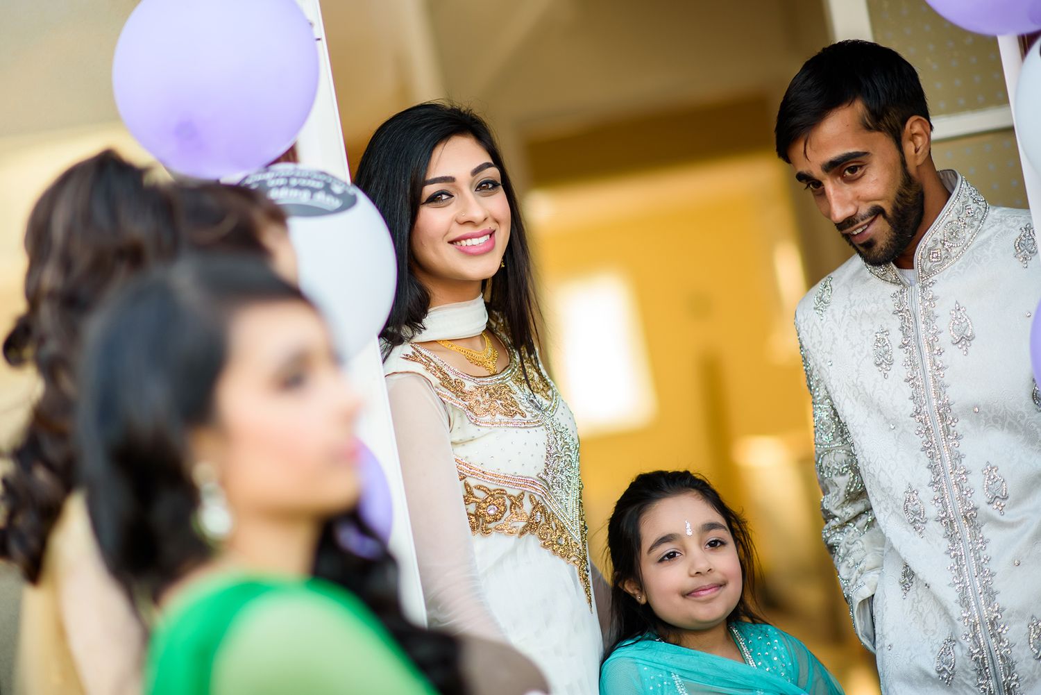 A festive family gathering with traditional outfits and purple balloons in the background.