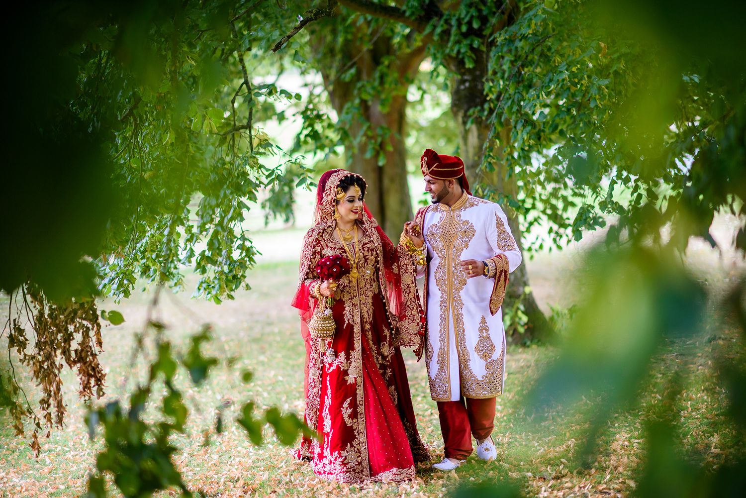 Artistic wedding photography through tree leaves showing couple in traditional Indian dress.
