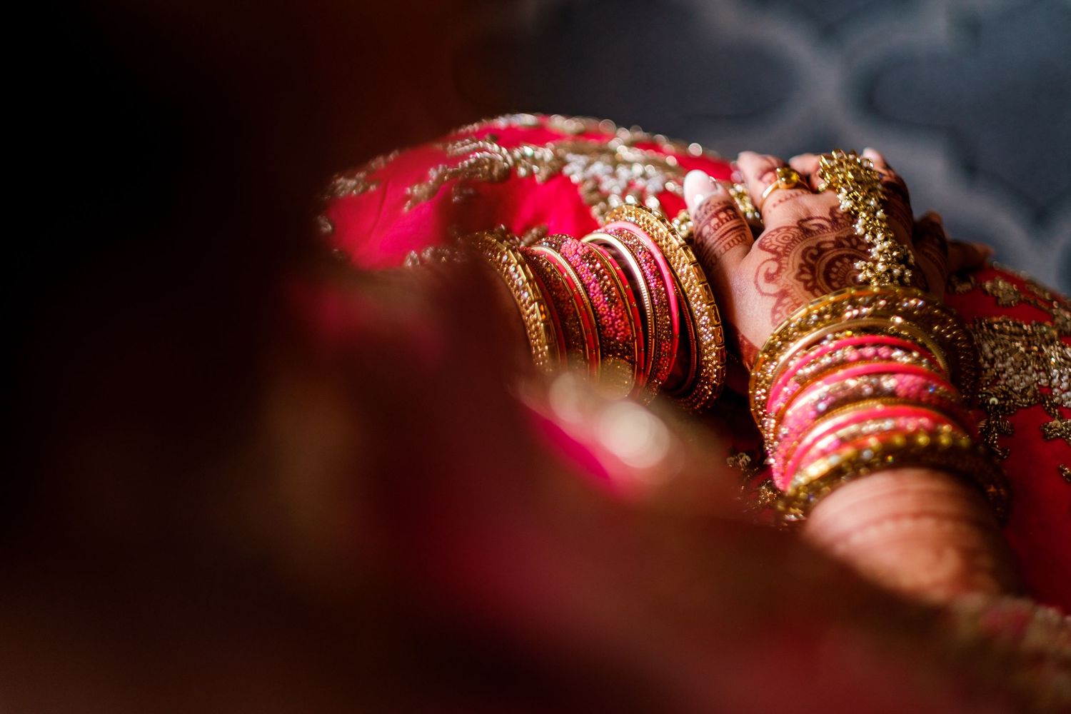 Close-up detail of intricate henna designs and red bangles on hands adorned with traditional Indian bridal jewelry.