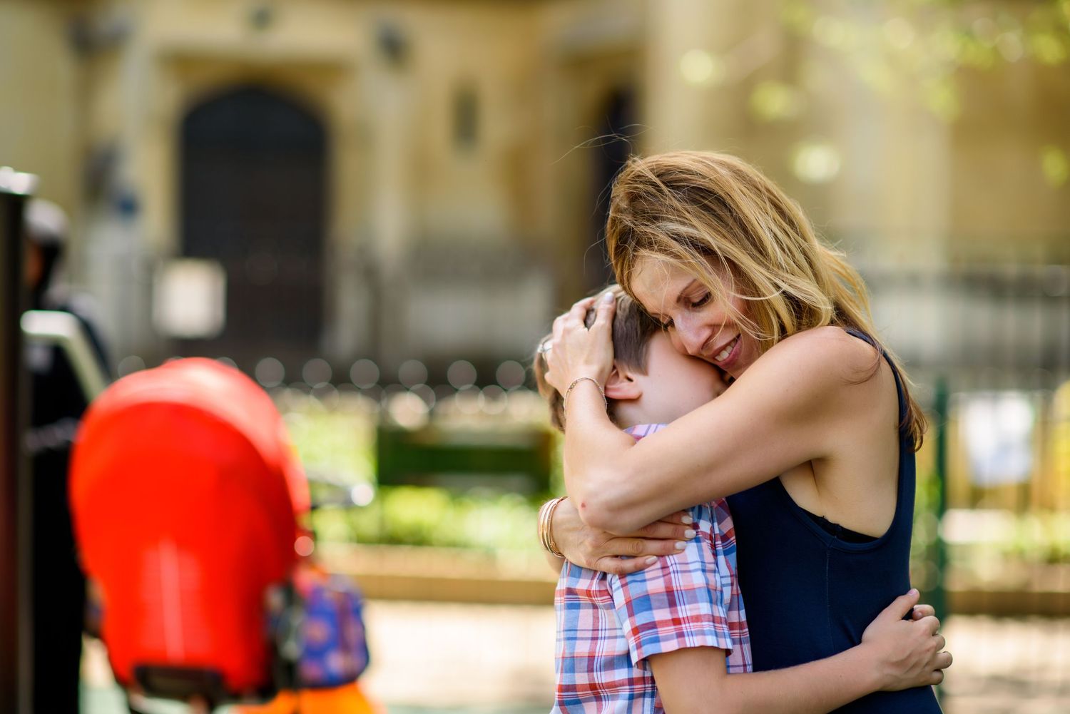 A tender moment of comfort and affection shared between an adult and child in a plaid outfit outside.