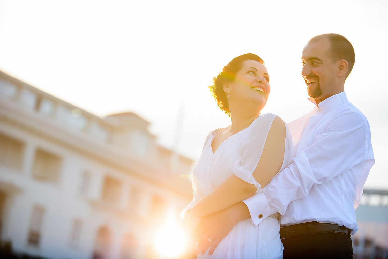 A couple sharing a romantic moment at sunset with a building in the background.
