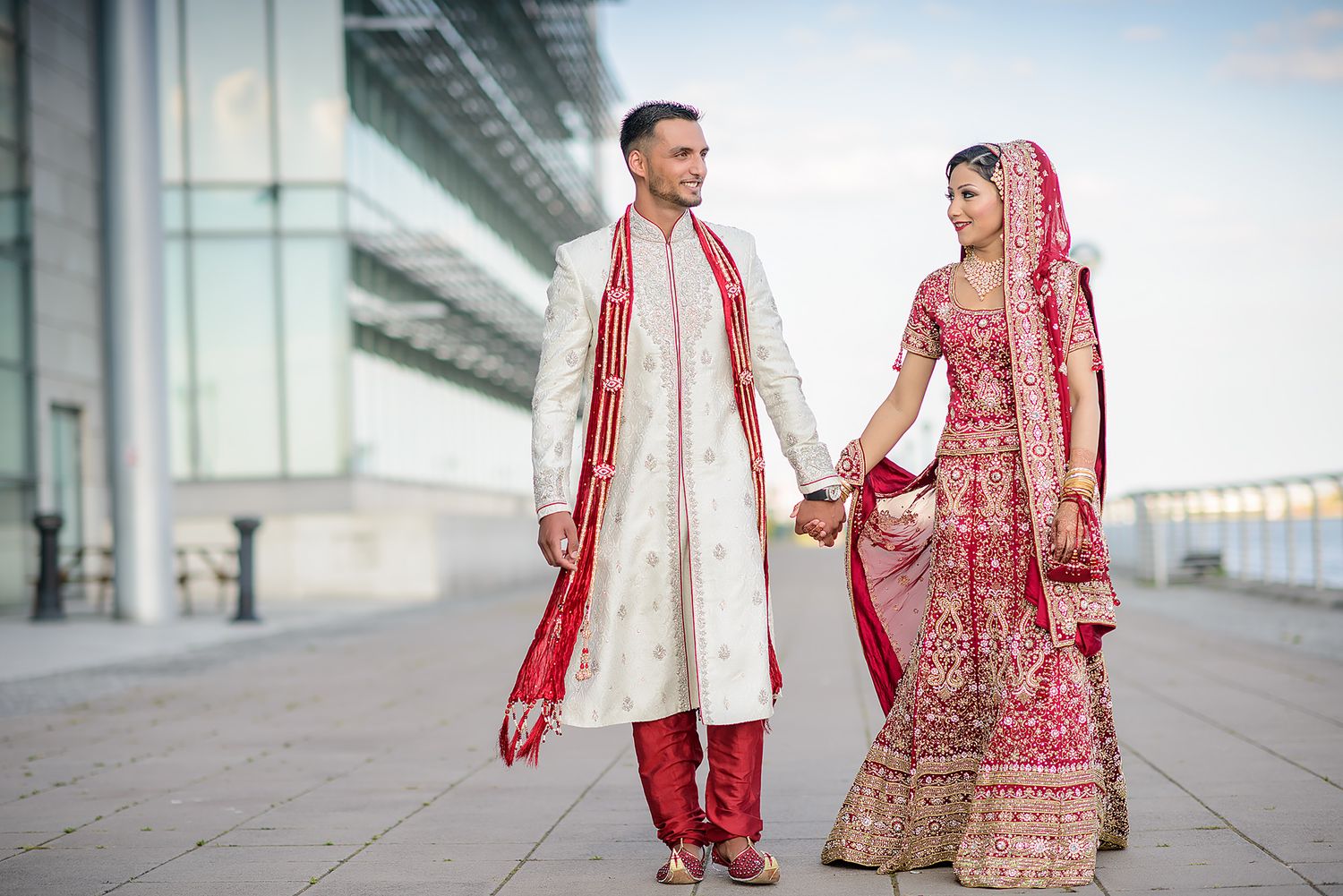 South Asian wedding couple walking together along modern building exterior.