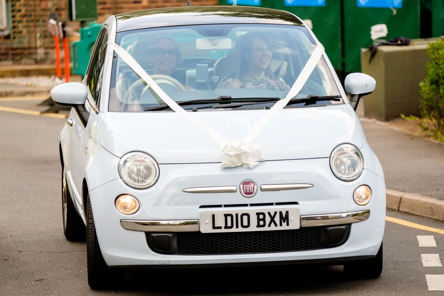 Classic white Fiat 500 wedding car decorated with ribbons parked on street.