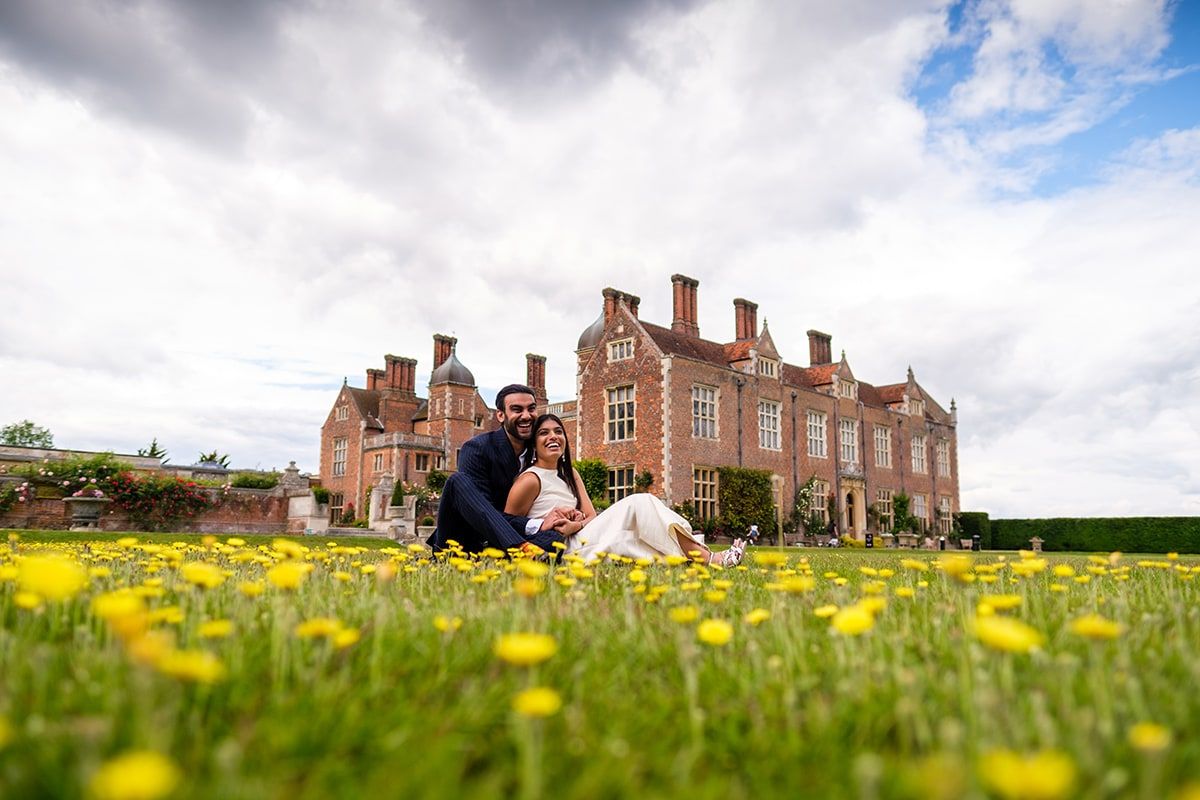 Couple relaxing in blooming meadow with stately brick manor house in background.