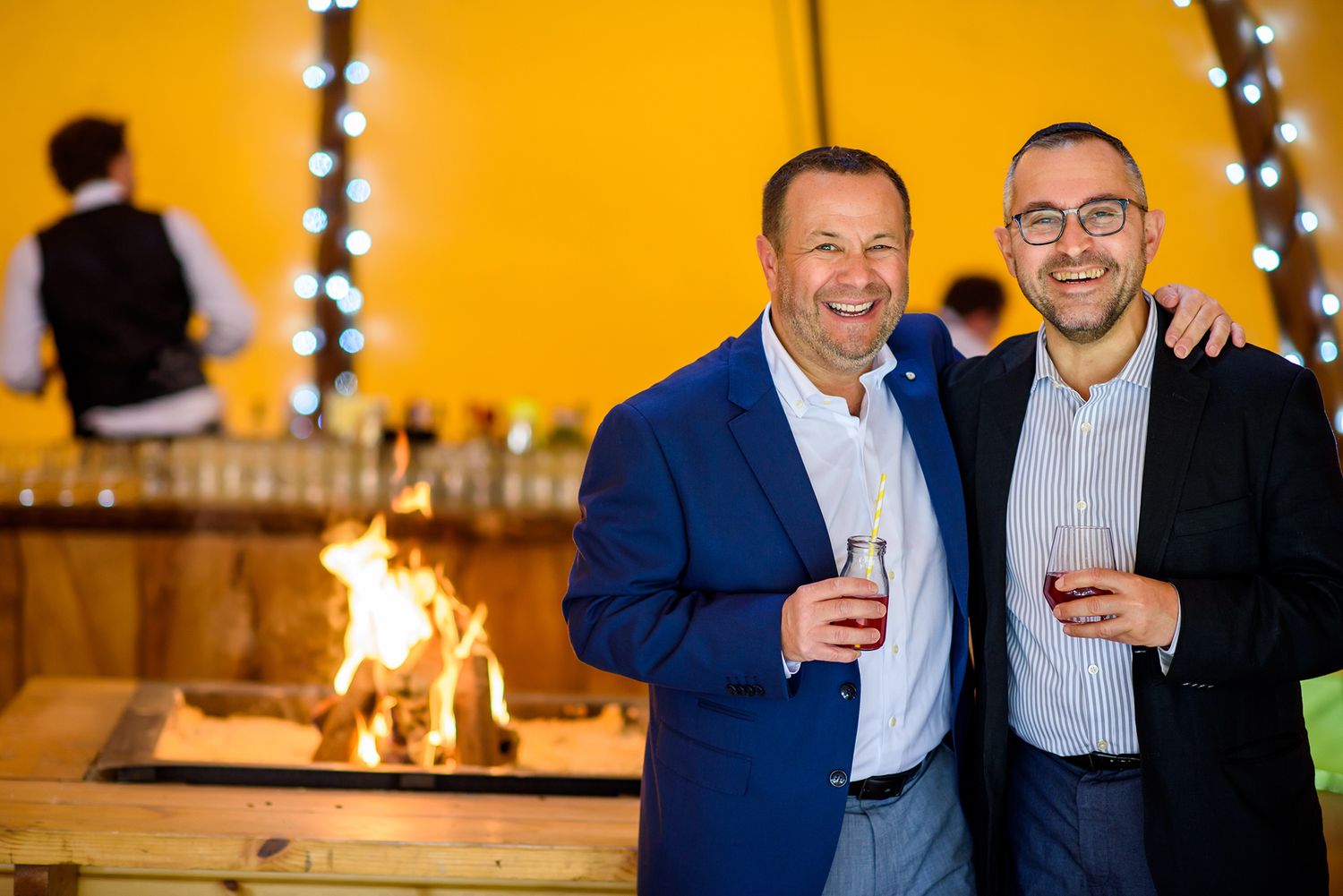Wedding guests enjoying drinks and conversation at an evening reception with warm lighting.