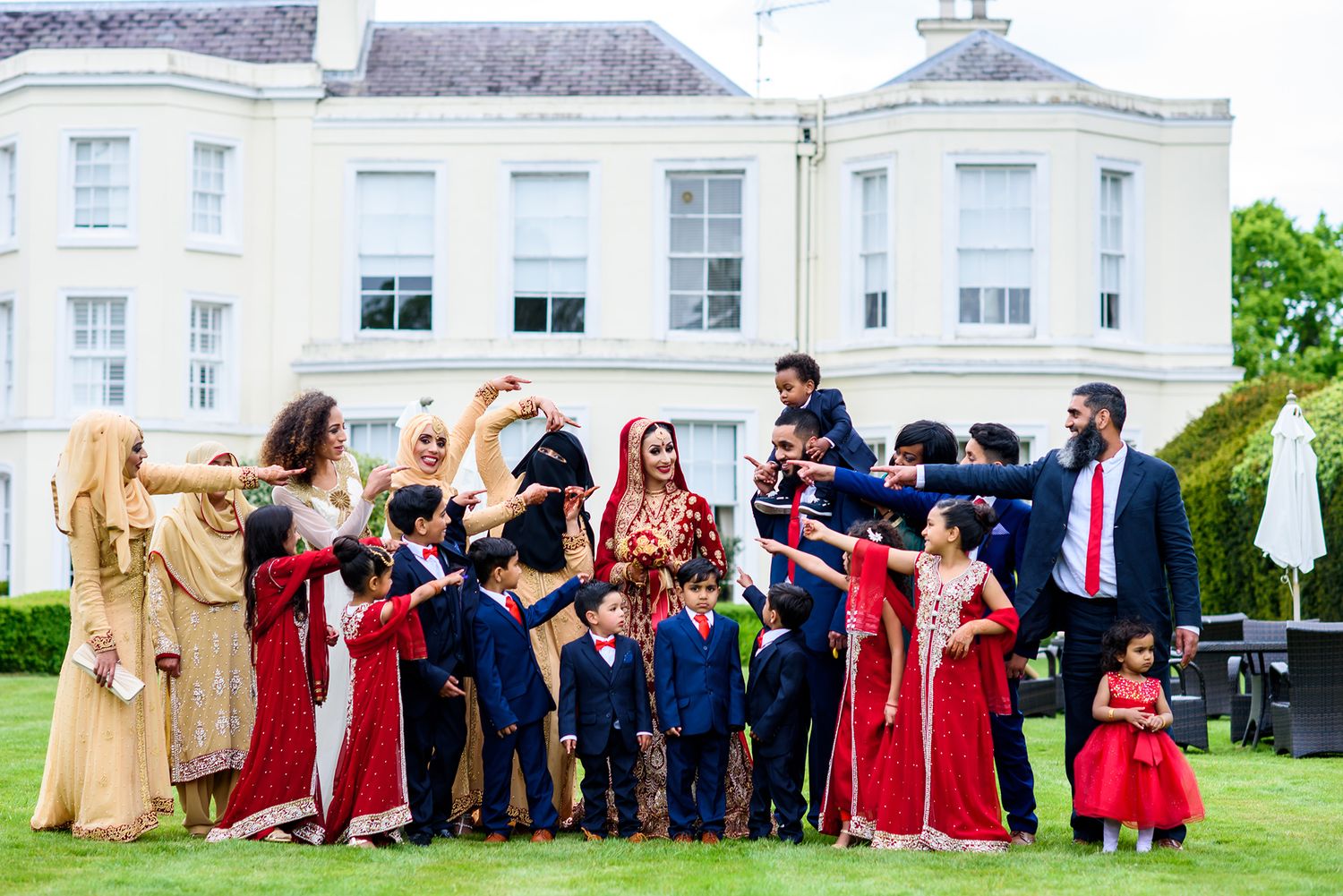 Wedding party celebrating on lawn outside elegant white building.