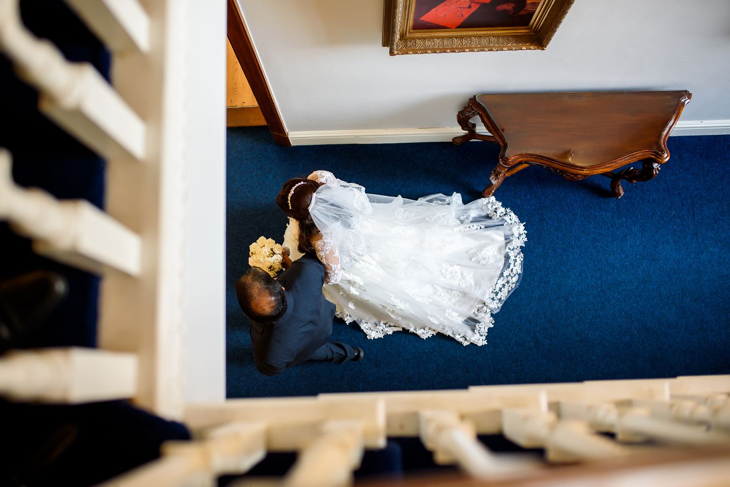 Interior hallway with white railings and blue carpeting viewed from above.