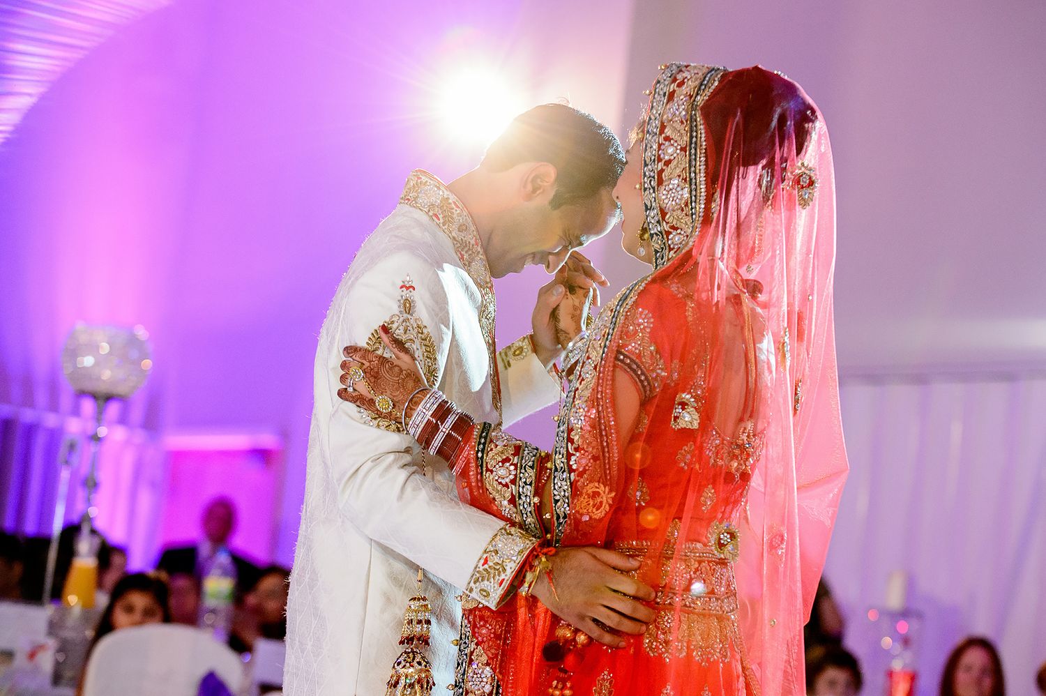 Traditional South Asian wedding ceremony with couple in white and red attire under purple lighting.