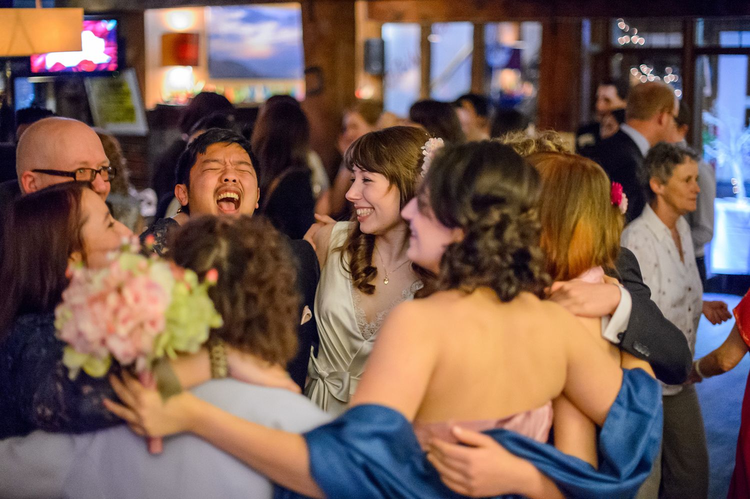 Party guests dancing and celebrating in crowded indoor venue with festive lighting.