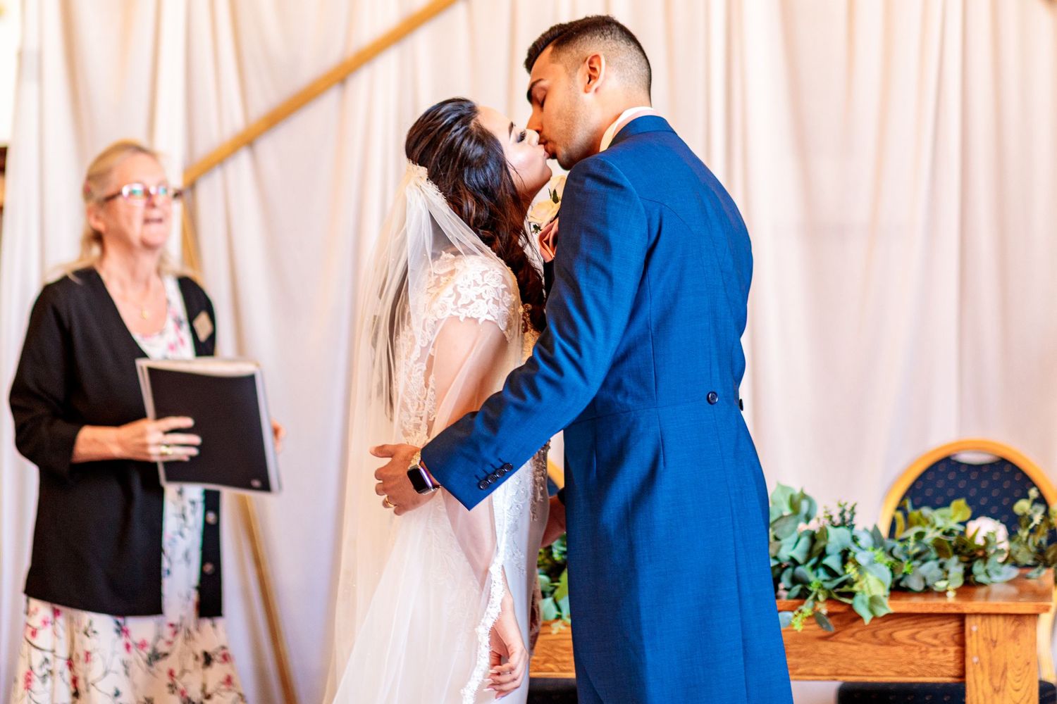 Wedding party members sharing emotional moments during reception with floral decor and white backdrop.