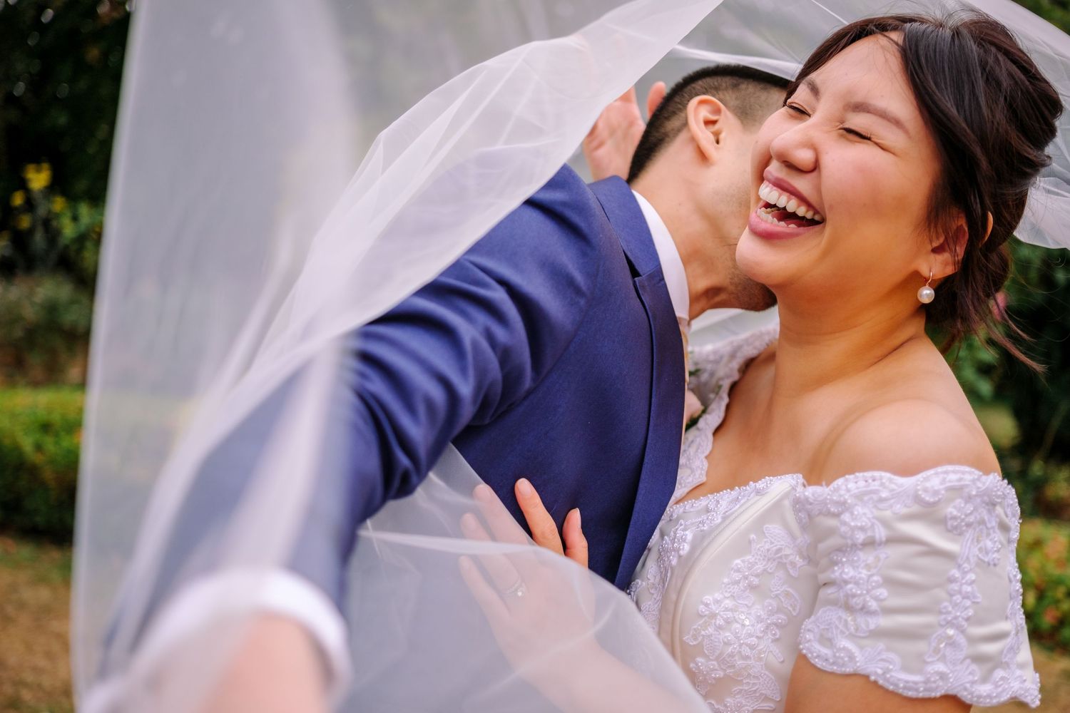 A joyful couple shares intimate moments in a garden setting wearing wedding attire.