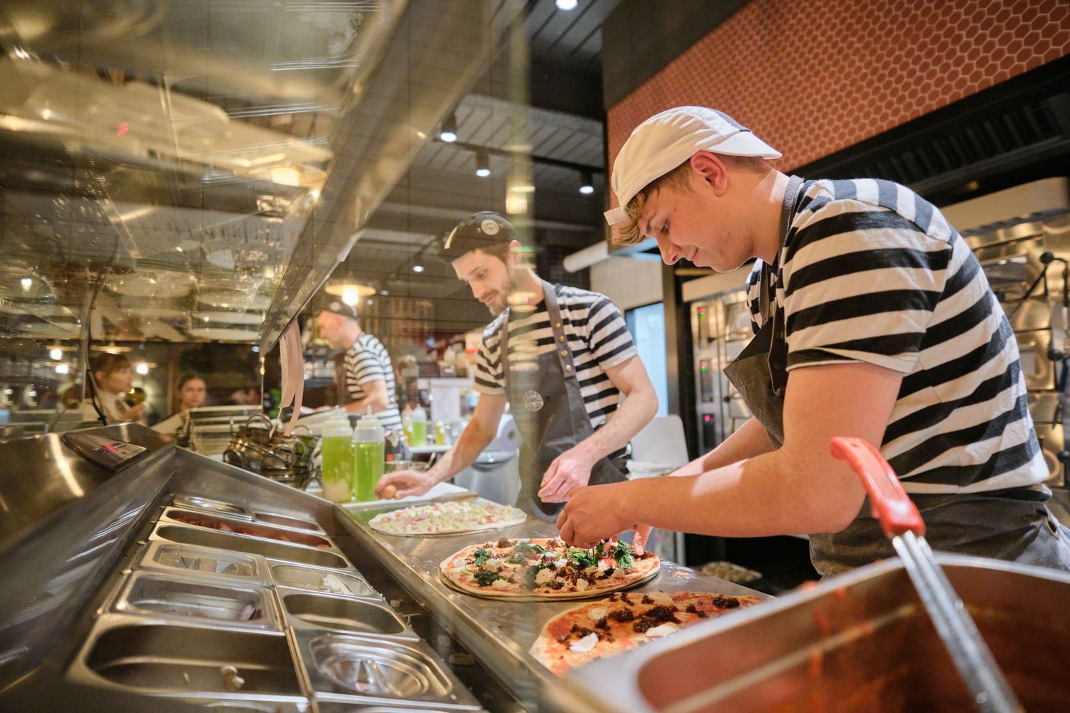 Restaurant staff preparing food at a commercial kitchen counter with stainless steel equipment.