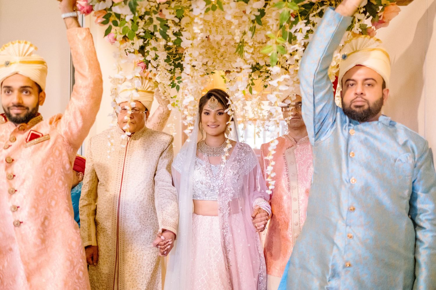 Wedding celebration with group wearing traditional South Asian attire under floral decor.