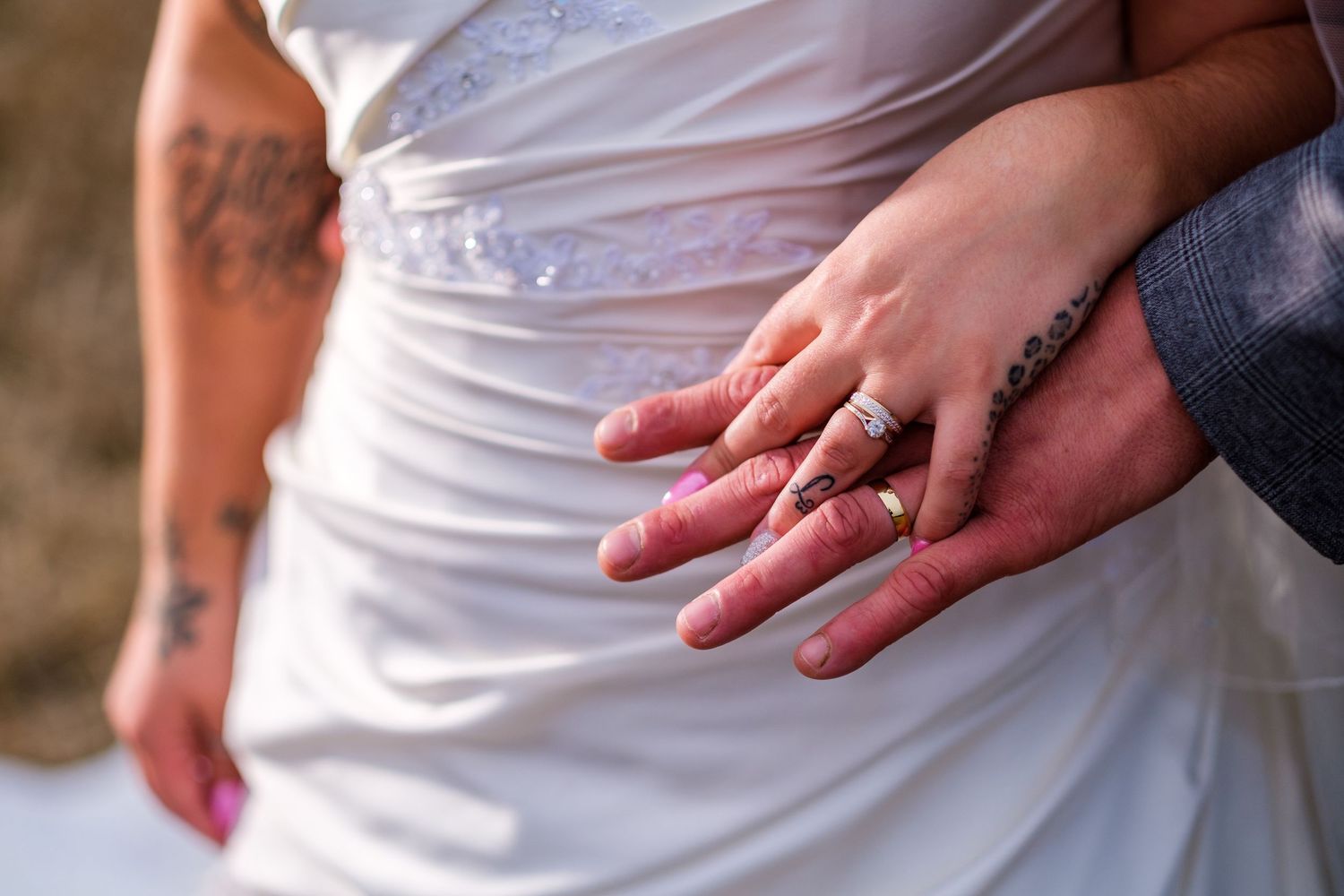 Detail shots of hands wearing wedding rings against white wedding dress fabric.