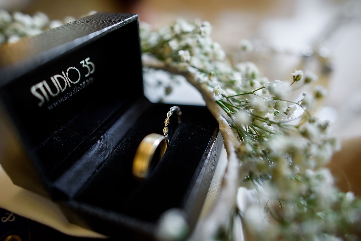 Wedding ring in black jewelry box with delicate baby's breath flowers.