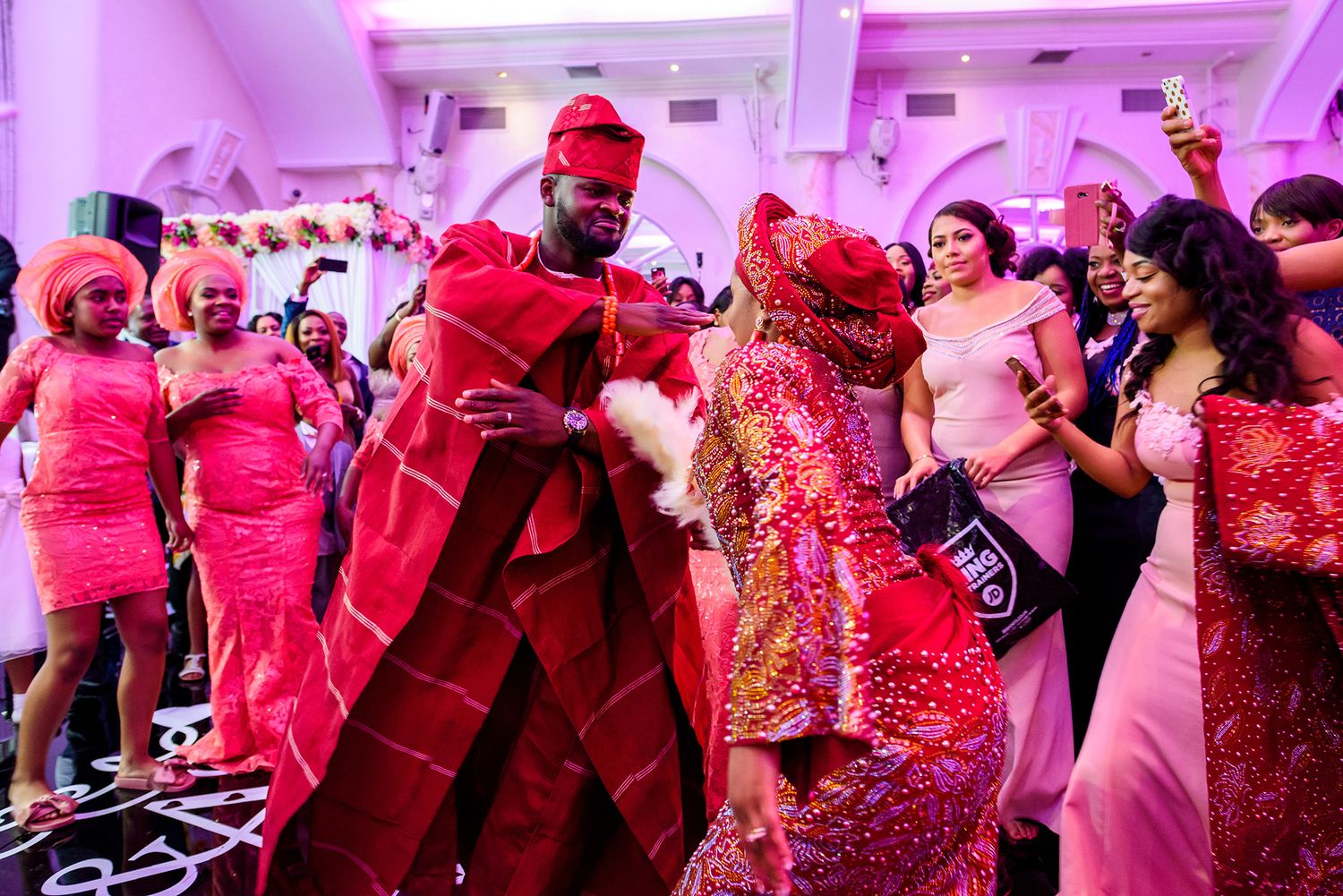 Wedding celebration with guests in coordinated red outfits dancing under purple lighting.