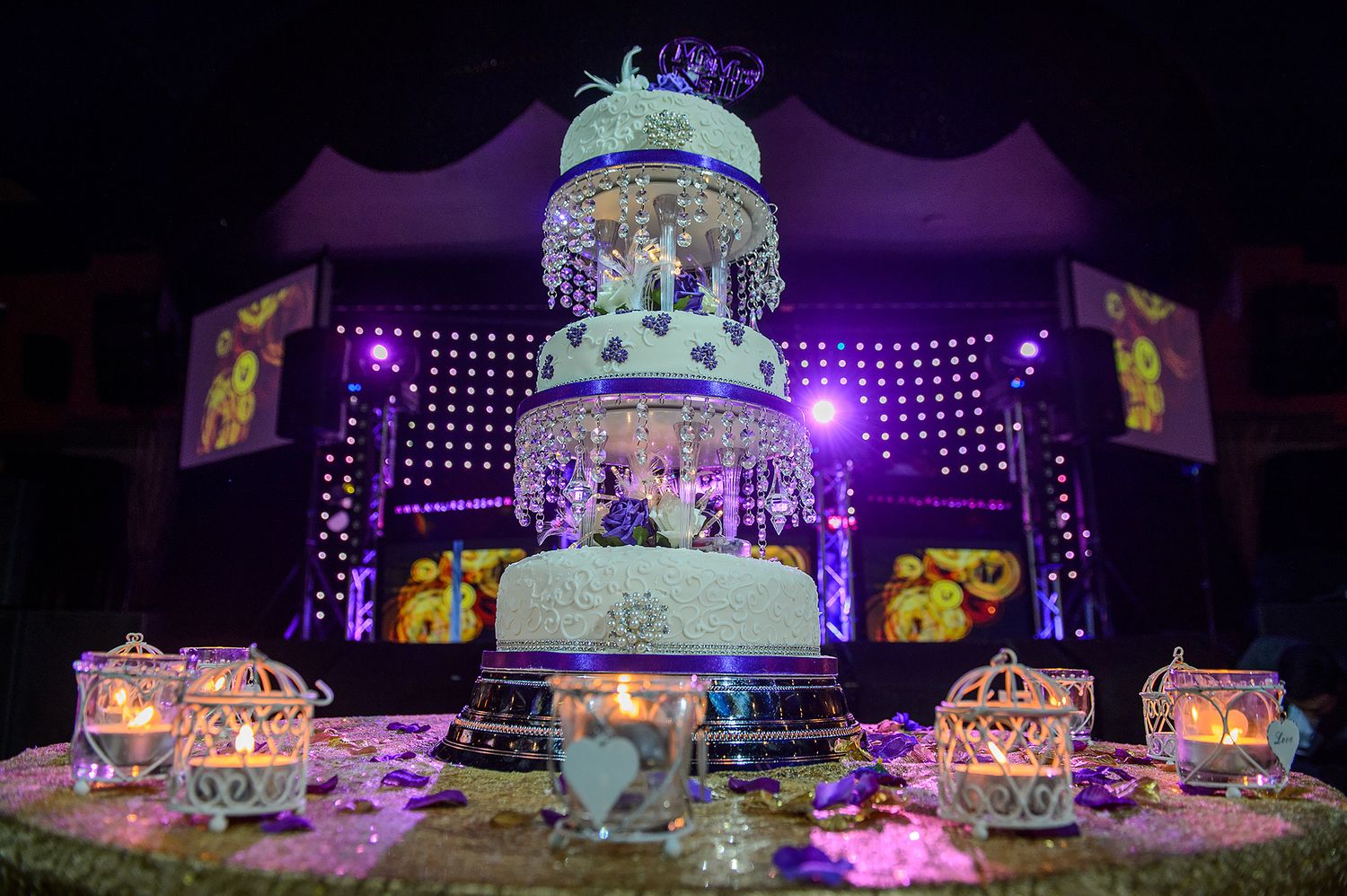 Elegant wedding reception setup with crystal decorations and purple mood lighting.