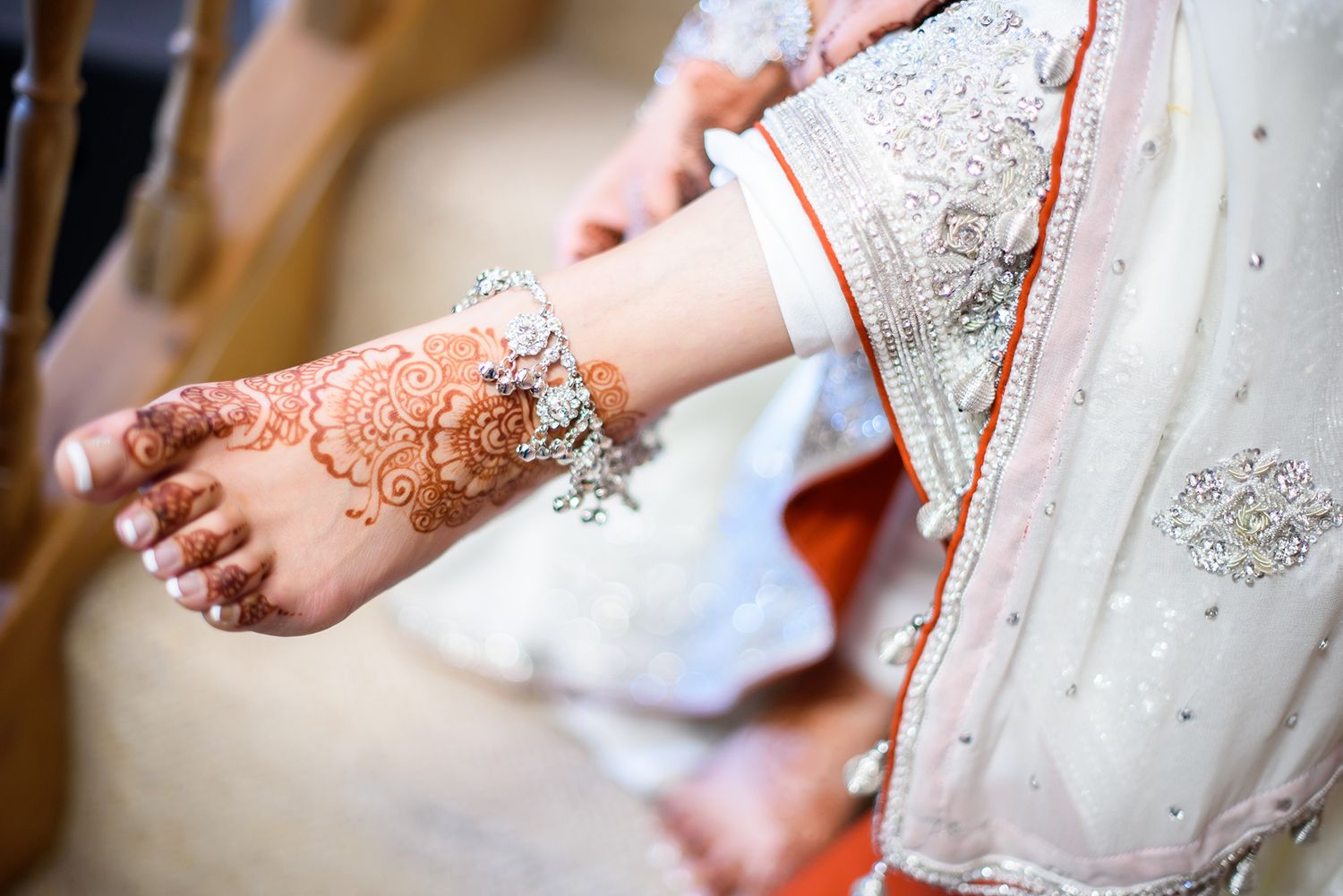 Intricate henna design decorates a bride's foot with white embroidered dress visible in frame.