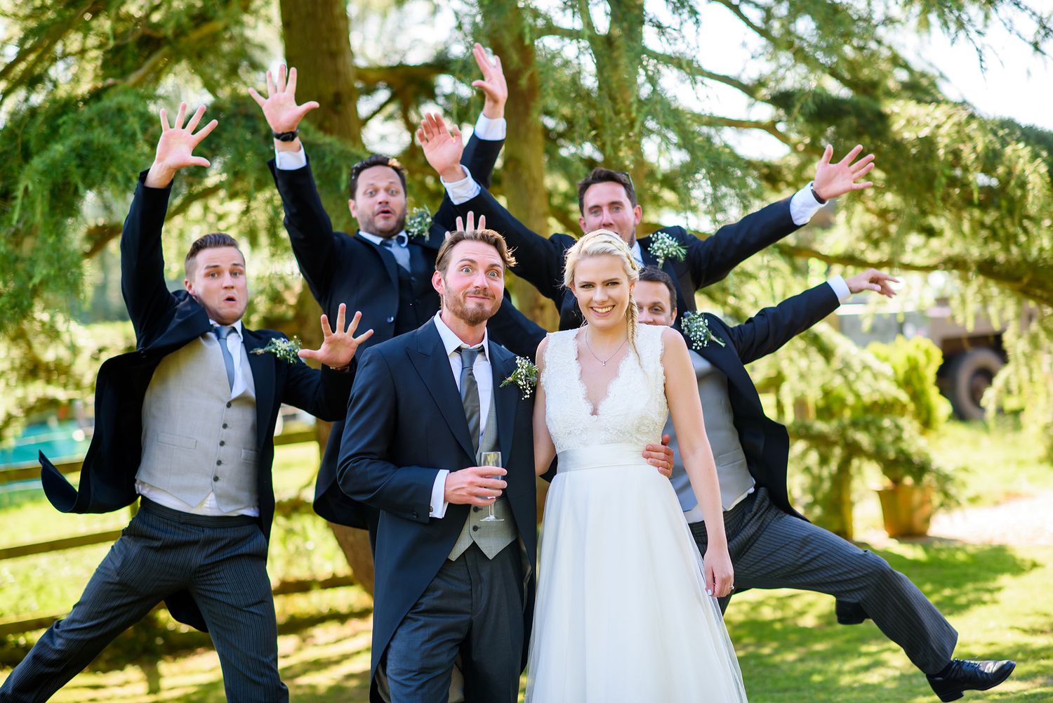 Joyful wedding party members jumping and celebrating outdoors in a garden setting.