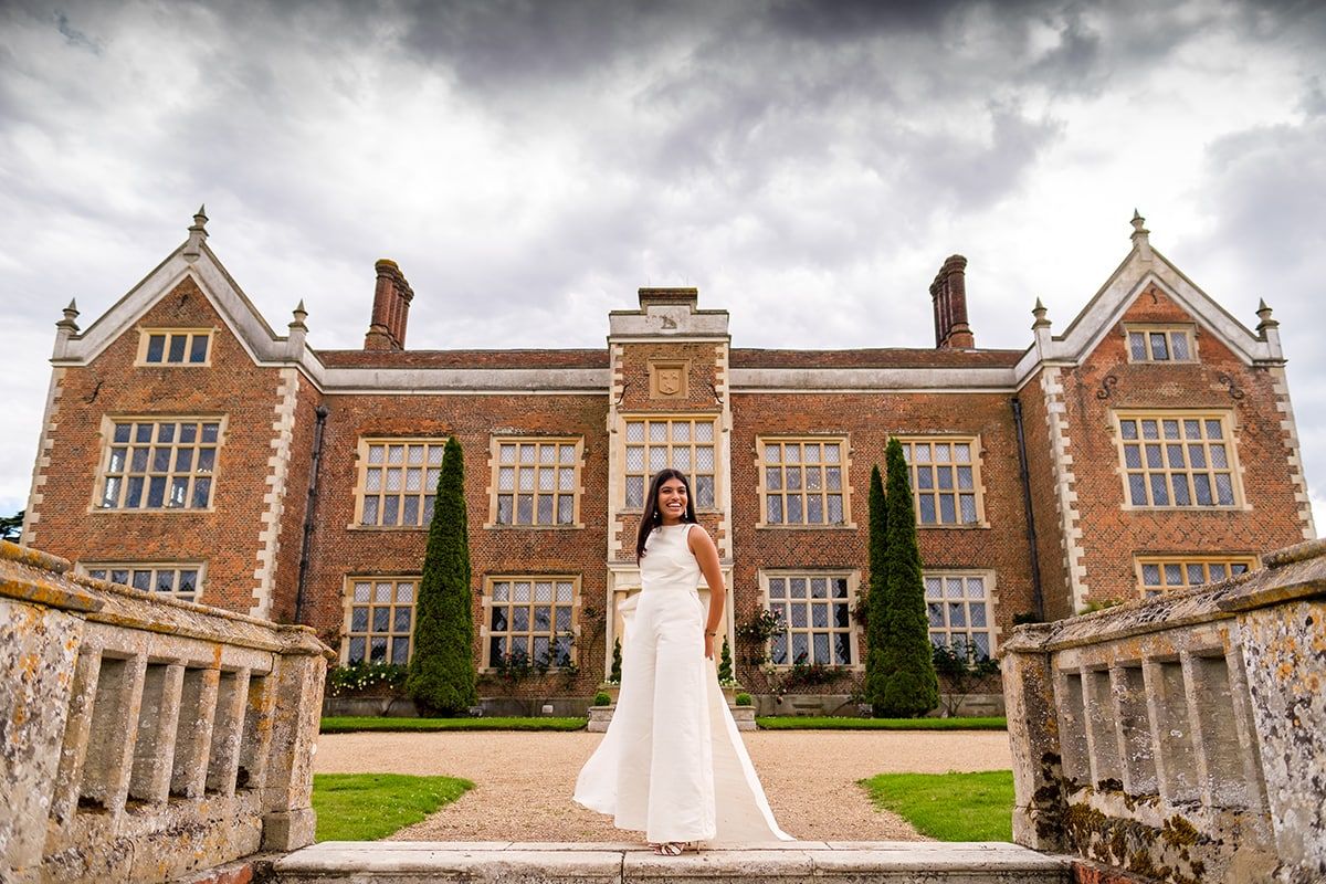 Elegant bridal portrait in front of a grand Victorian brick mansion under dramatic cloudy skies.