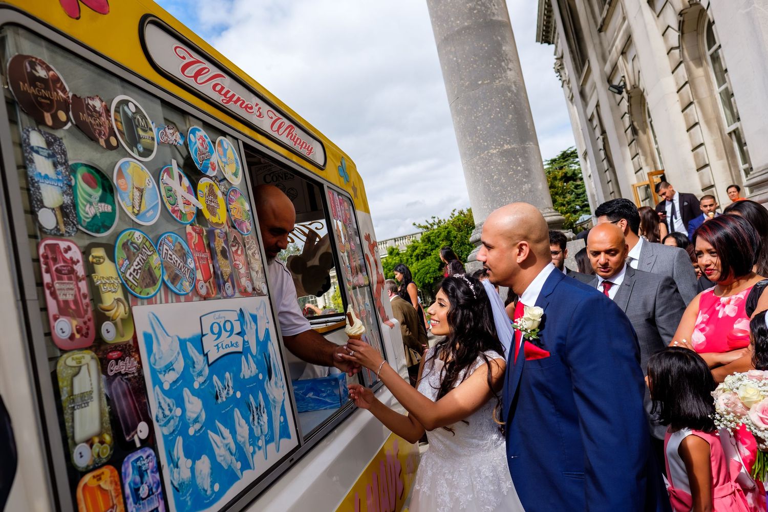 Wedding guests gather outside a building with graffiti-covered walls.
