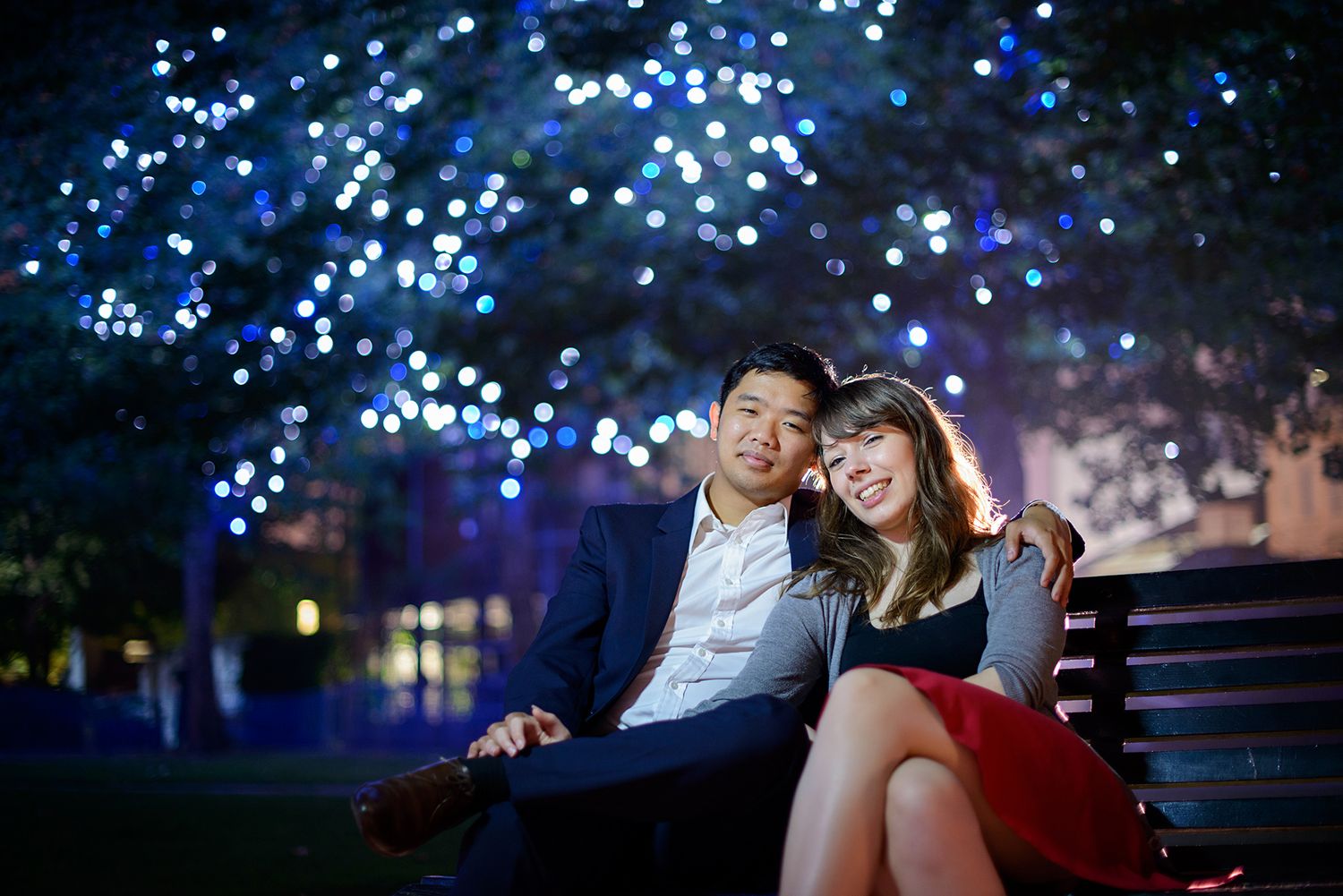 Couple relaxing on bench under twinkling blue lights at night.