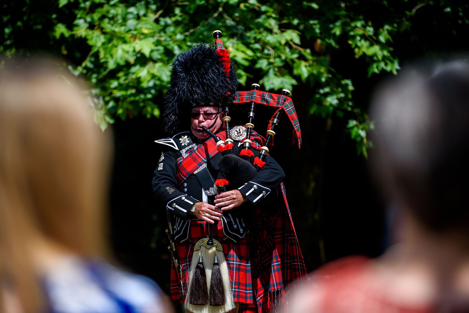 Scottish bagpiper plays traditional music at outdoor wedding ceremony.