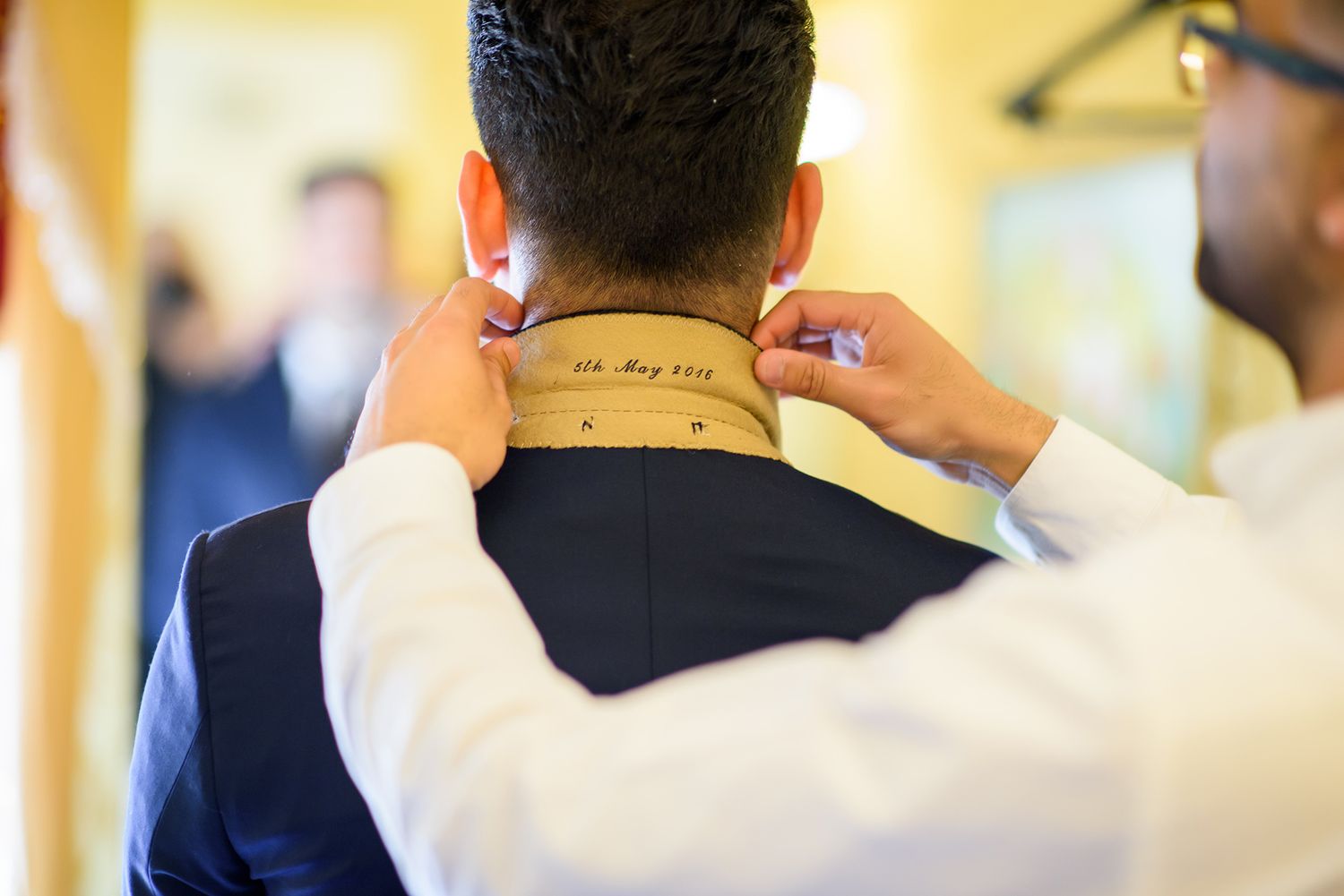 Close up of hands adjusting collar and tie of a formal navy suit jacket.
