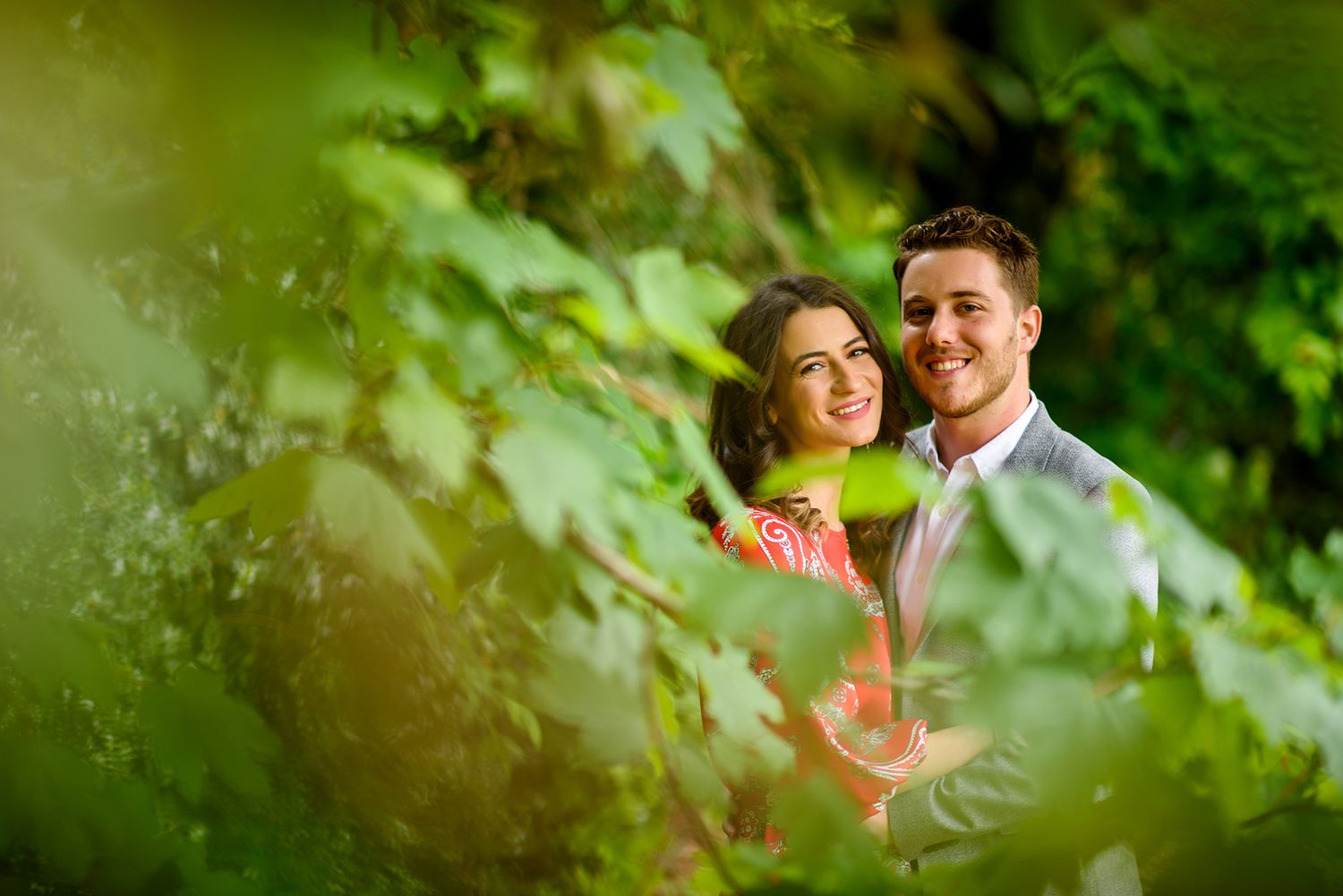 A romantic portrait framed by green leaves during an engagement session.