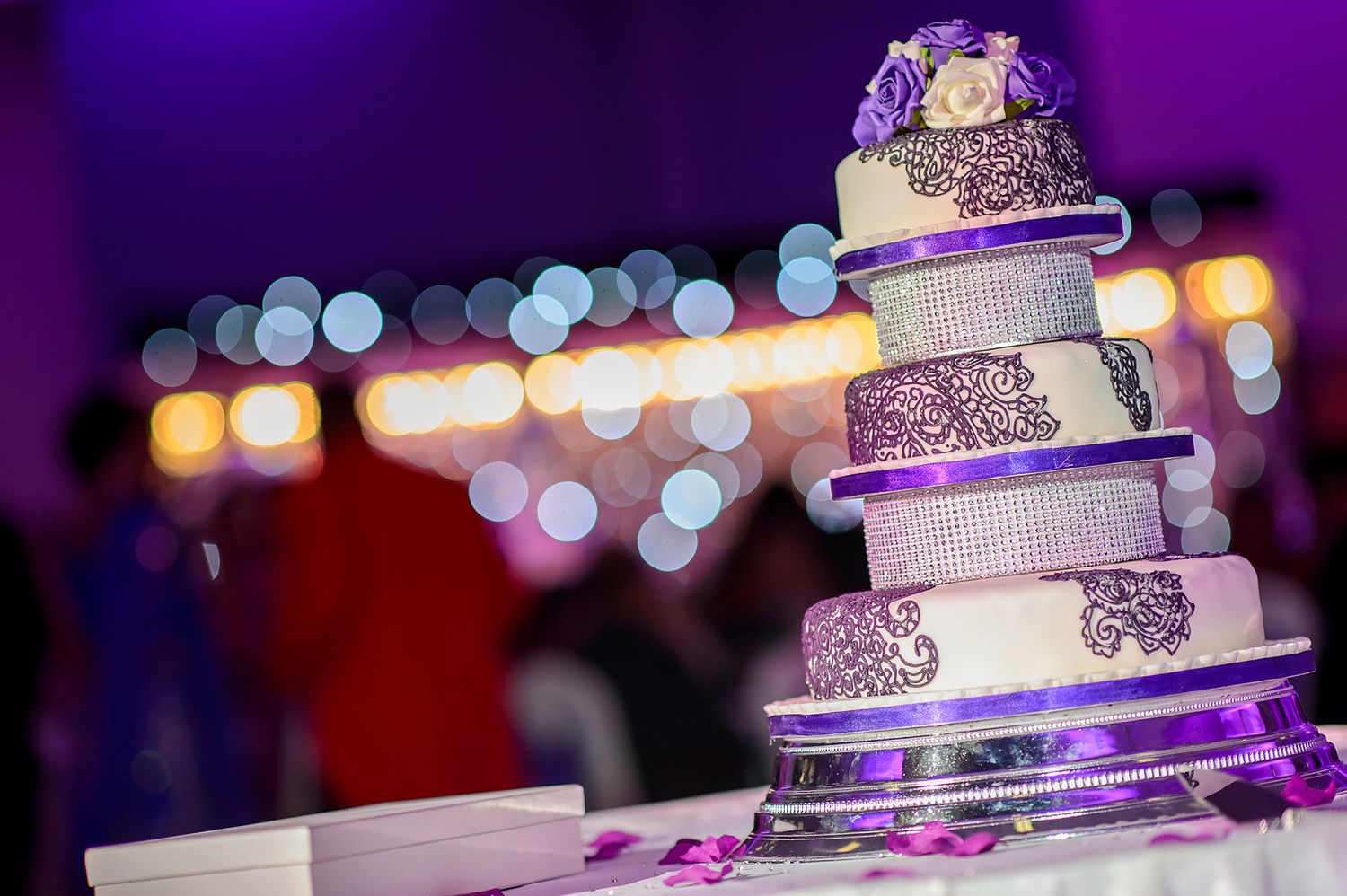 Elegant tiered wedding cake with purple lighting and bokeh background.
