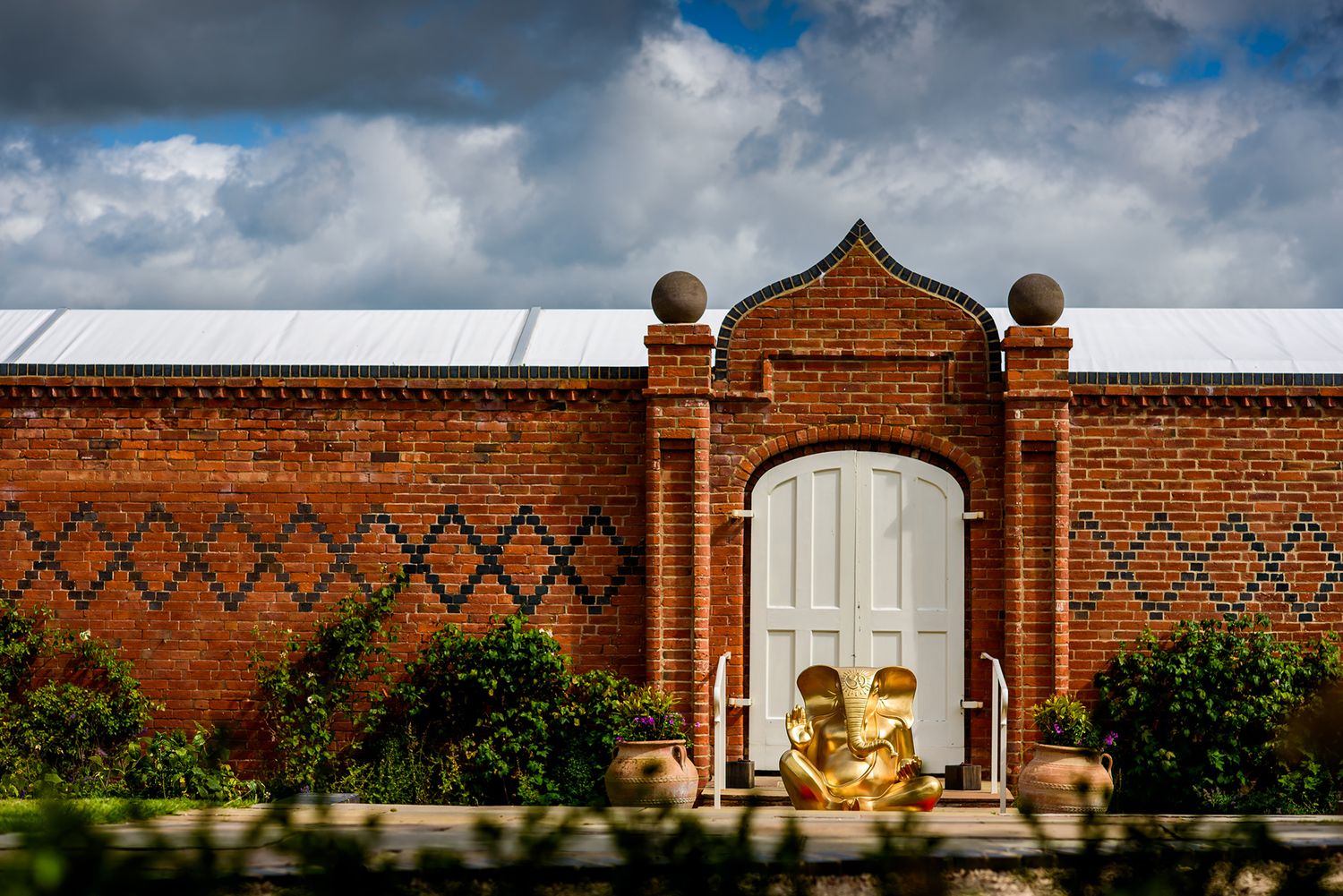 Red brick wall architecture with ornate details against cloudy blue sky.