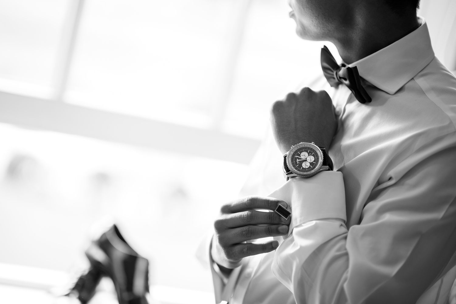 Close-up of formal attire showing white shirt cuff, watch and bow tie.