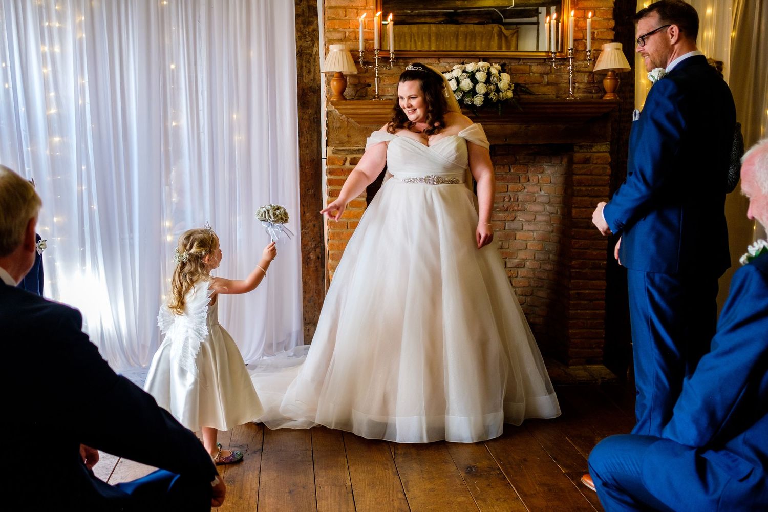 Elegant wedding scene with bride in white tea-length dress and groom in navy suit dancing in rustic brick venue.