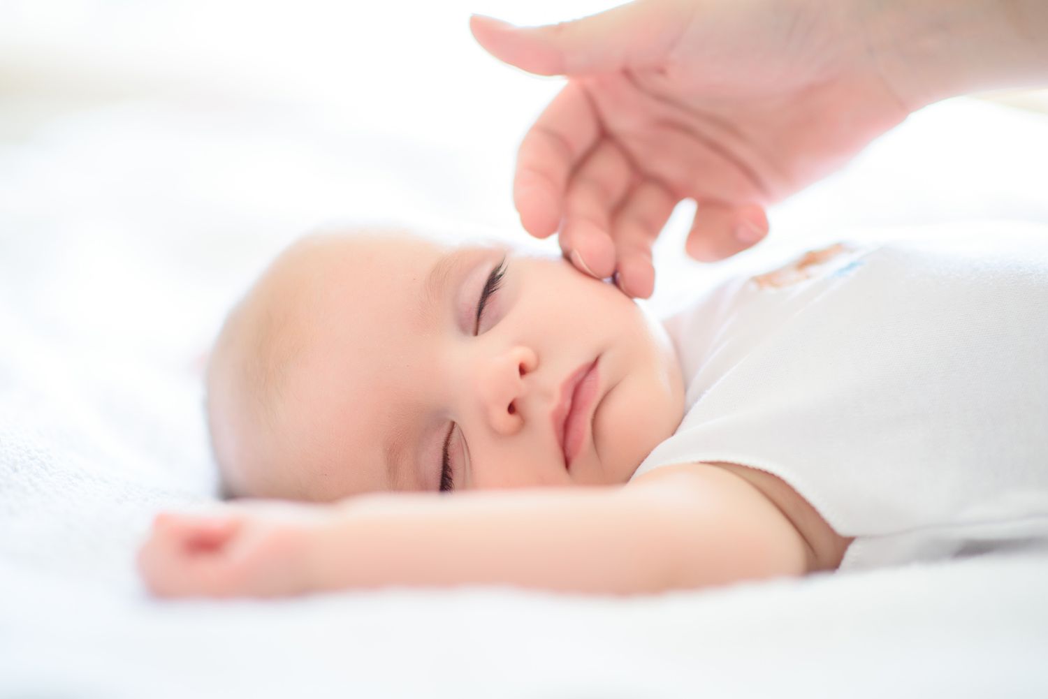 Close-up of gentle hands tenderly touching a sleeping baby wrapped in white linens.