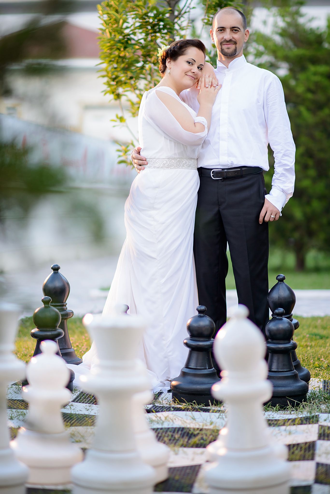 Newlyweds pose together behind large chess pieces on their wedding day.