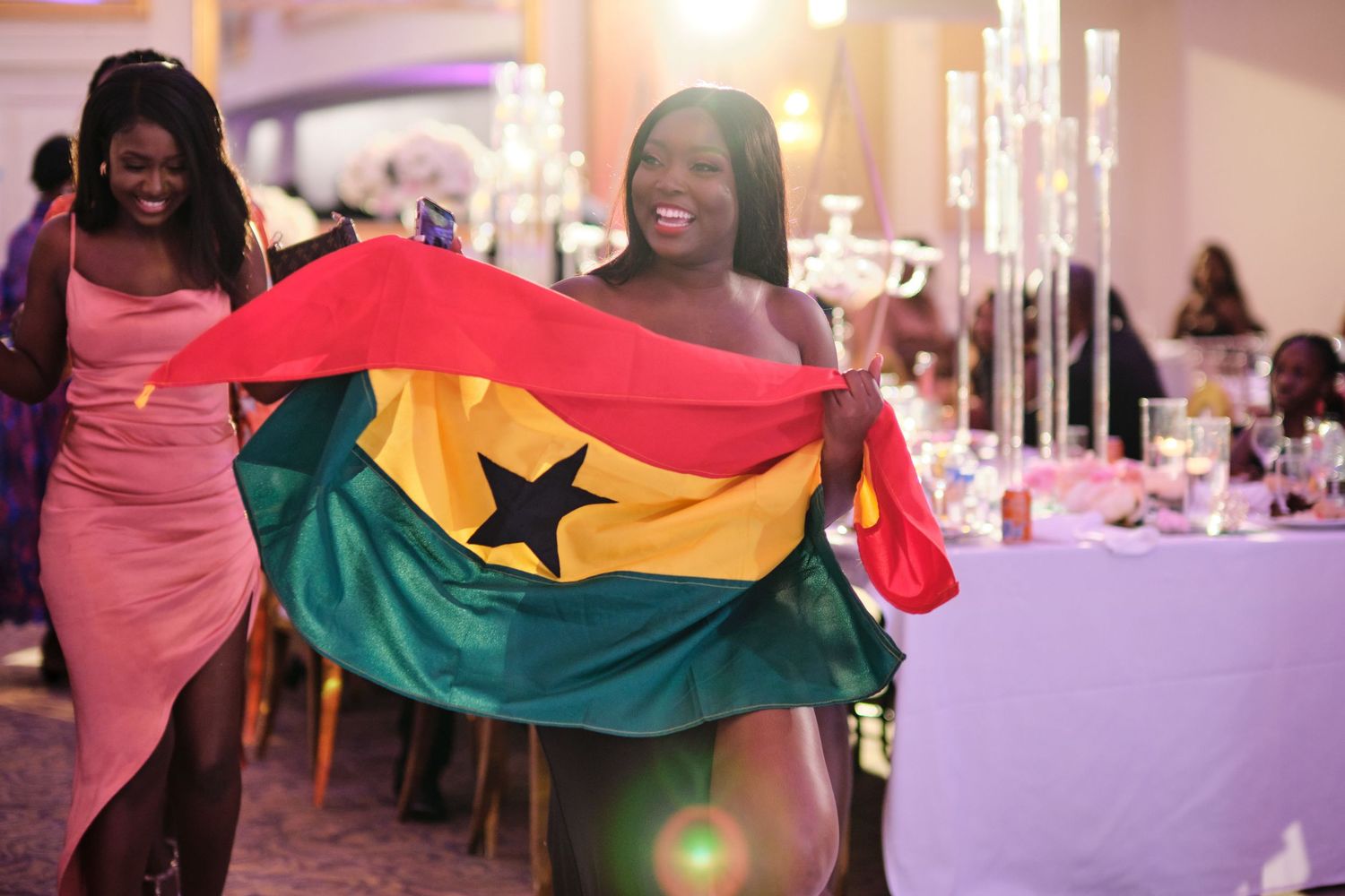 Wedding celebration with guests holding up Ghana flags during a festive reception party.
