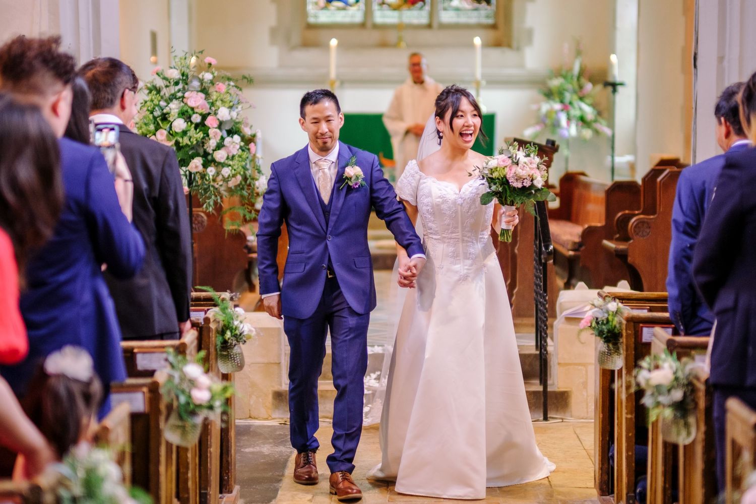 Guests celebrate at an elegant indoor wedding ceremony with floral arrangements and decorative lighting.
