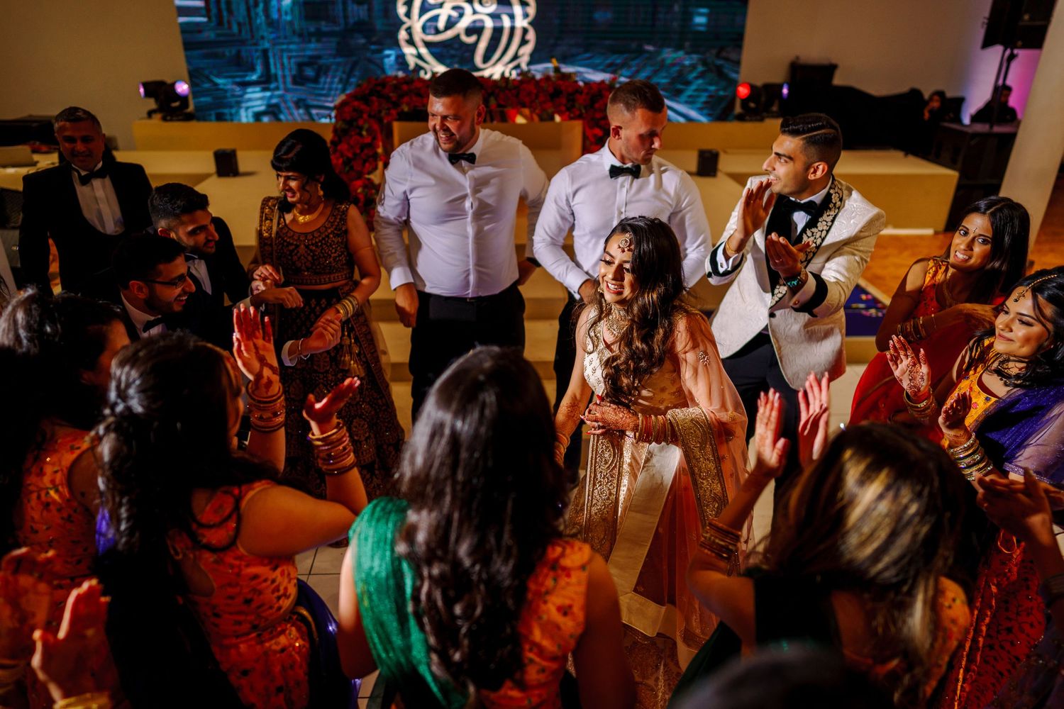 Wedding guests dance and celebrate on a dimly lit dance floor during an energetic reception party.