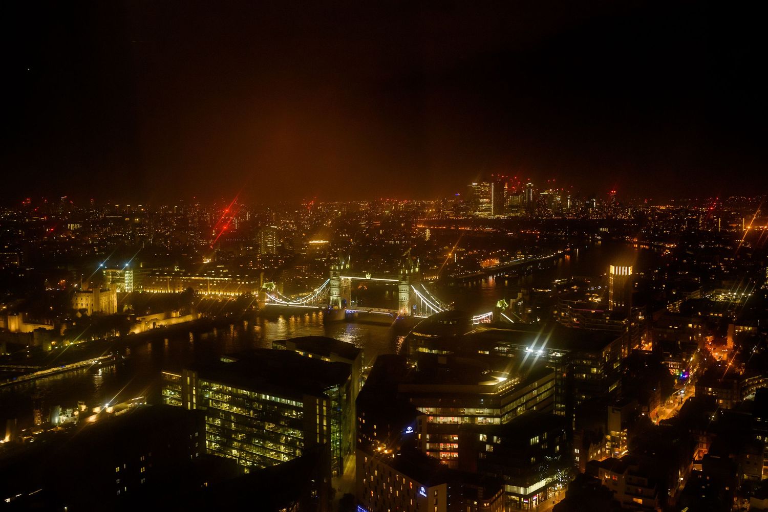Nighttime cityscape view with illuminated buildings and bridges.