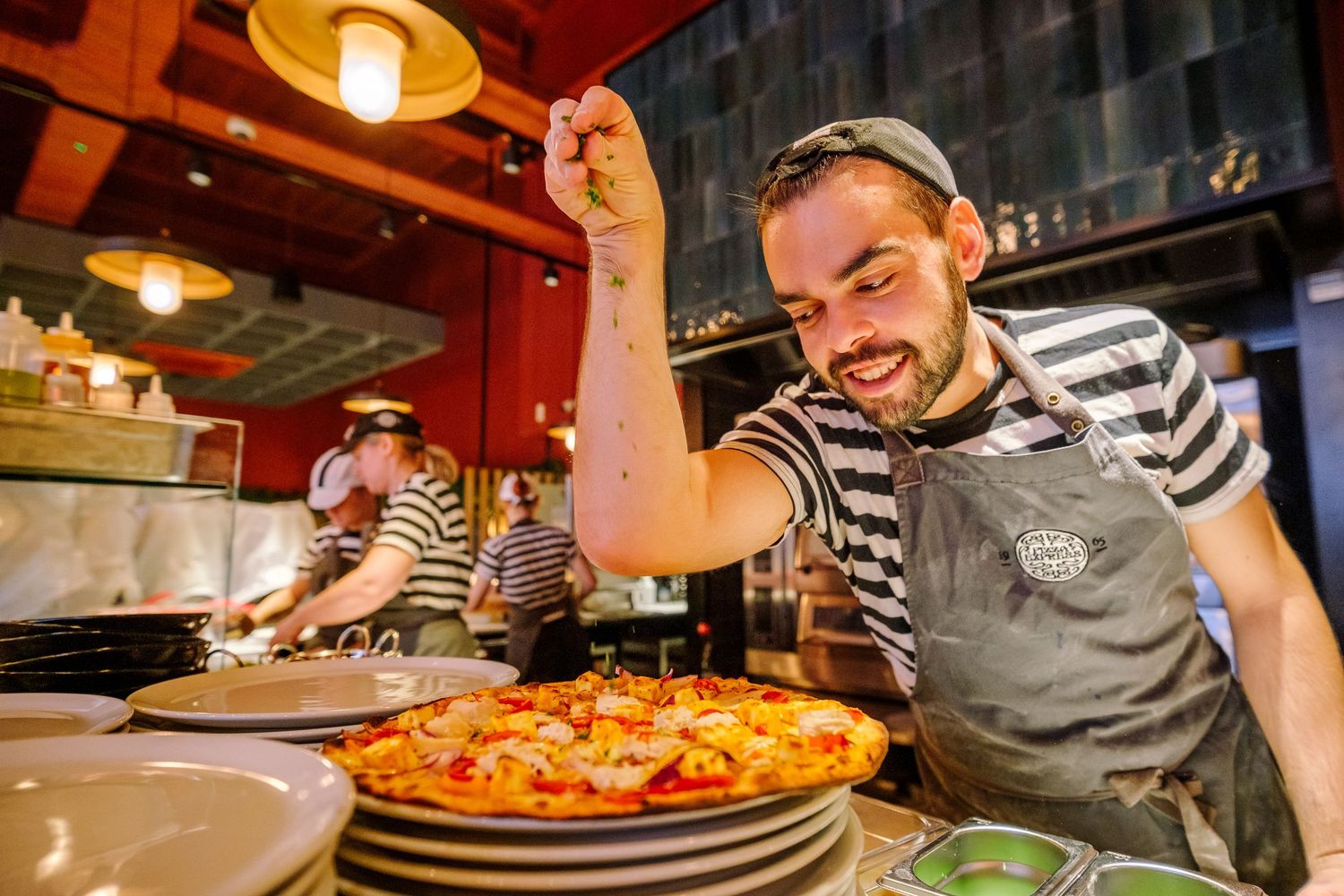 Pizza chef in striped shirt working with dough in a restaurant kitchen.