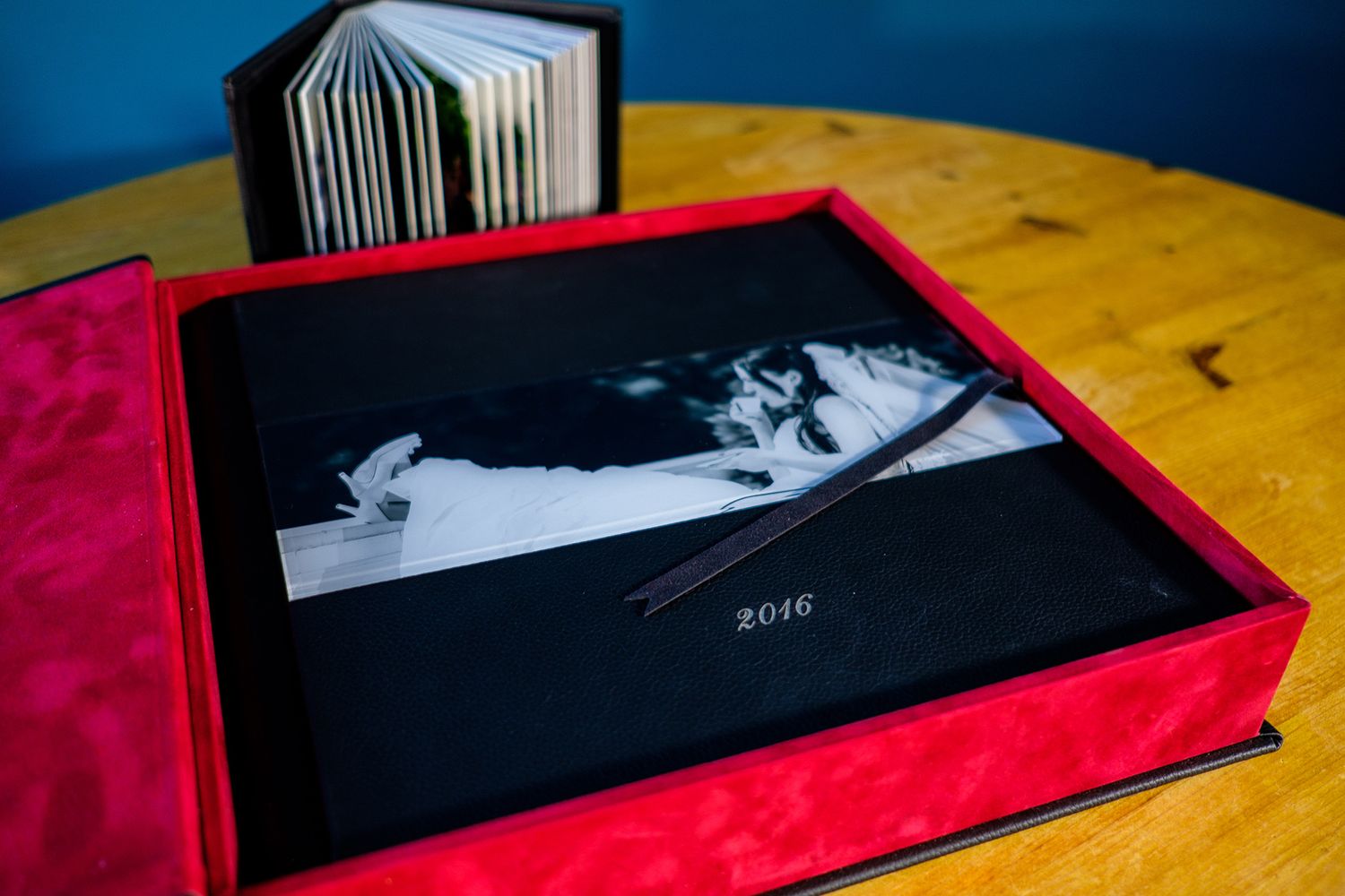 Wedding album with red binding photographed on wooden table with blue wall background.