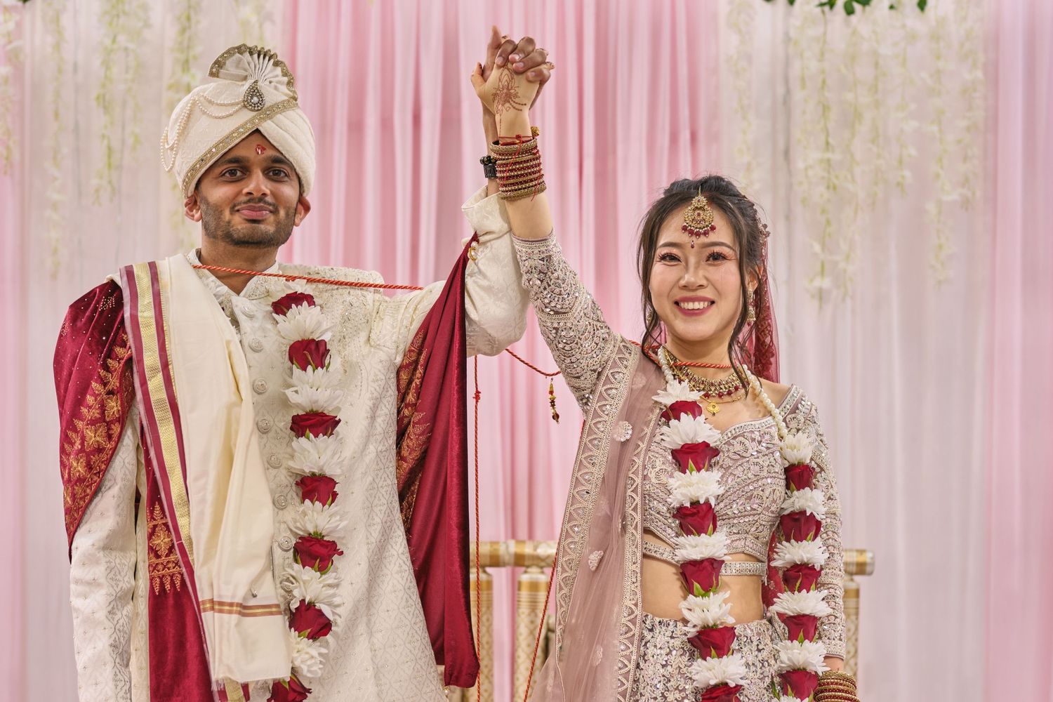 Traditional Indian wedding ceremony with couple in red and white attire exchanging garlands under decorative mandap.